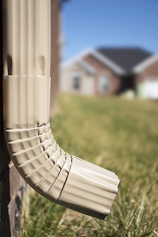 closeup of a light tan downspout on a brick home